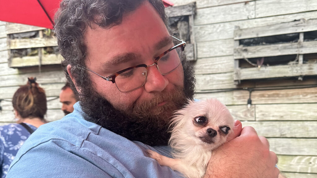 Gabe from Cabin Companions holding a small dog outdoors, reflecting the personalized, one-on-one care pets receive during their travels.