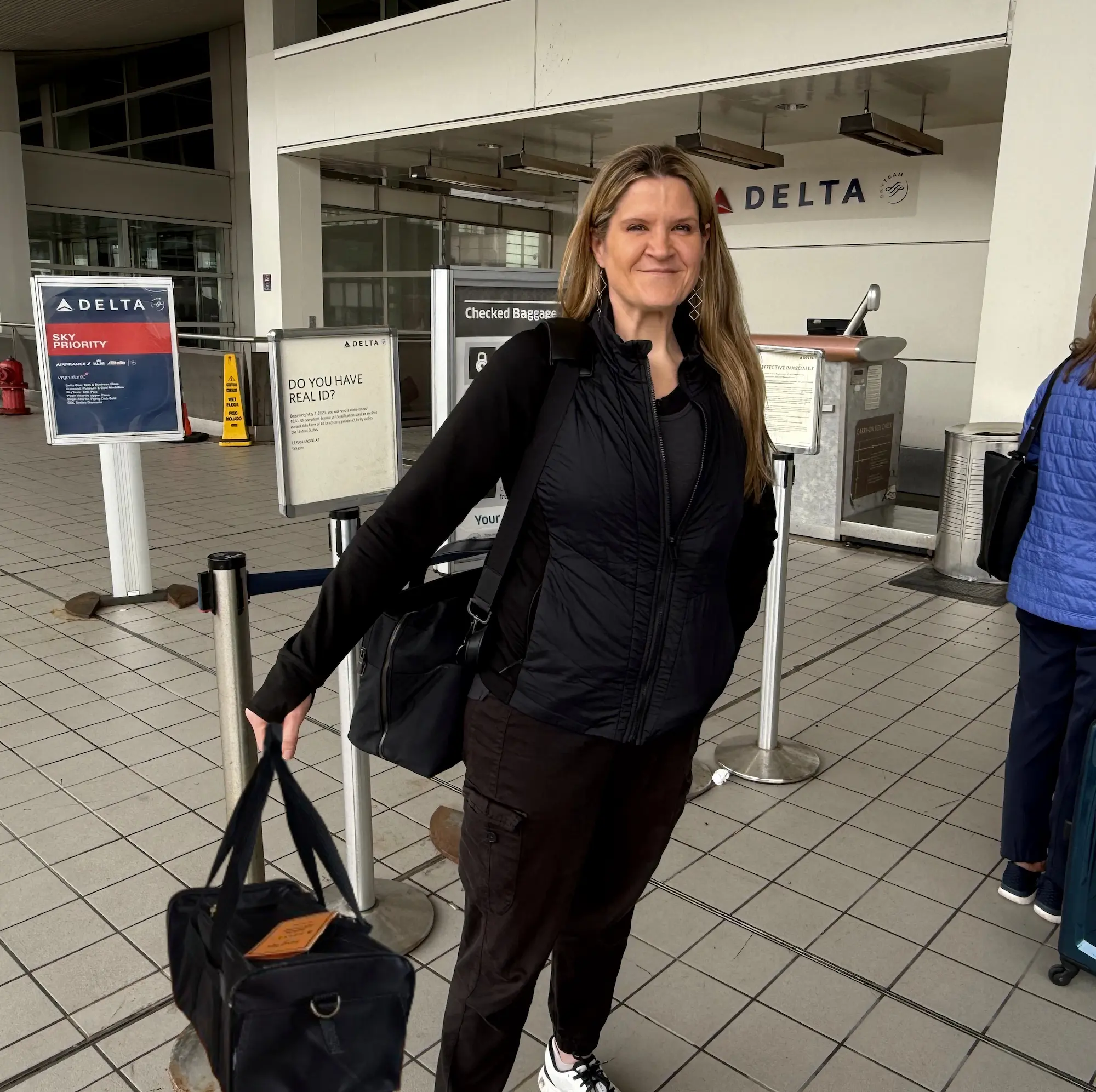 Monica standing at the Delta terminal with a soft-sided cat carrier, preparing for in-cabin pet travel.